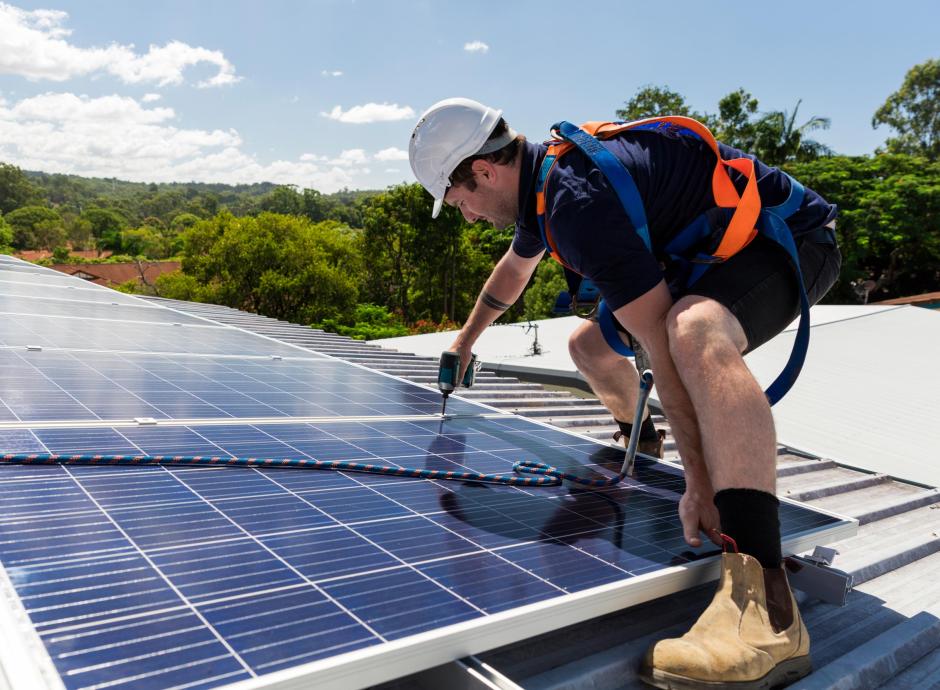 Solar panel technician with drill installing solar panels on roof on a sunny day